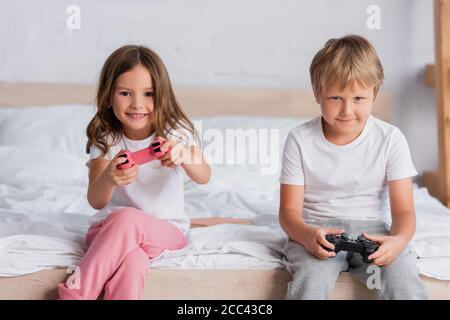 KIEW, UKRAINE - 21. JULI 2020: Aufgeregt Mädchen und fokussierten Bruder in Pyjamas spielen Videospiel im Schlafzimmer Stockfoto