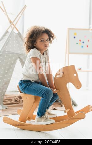 Lockiges afroamerikanisches Kind, das auf einem hölzernen Schaukelpferd sitzt Zu Hause Stockfoto