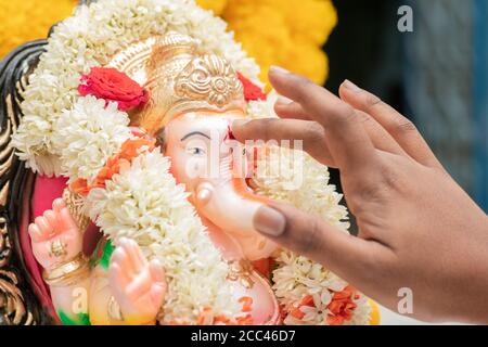 Nahaufnahme der Hände, die Tilak oder Kumkum auf Lord Ganesha während der indischen religiösen ganesha oder vinayaka Chaturthi Festzeremonie anwenden. Stockfoto