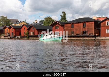 Hellgrünes Motorboot, das an den Holzlagerhäusern der Altstadt im Fluss Porvoonjoki in Porvoo, Finnland, vorbeifährt Stockfoto