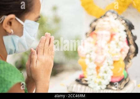 Mädchen Kind in medizinische Maske beten durch Schließen der Augen in Vorderseite von Lord Ganesha während Ganesha oder vinayaka Chaturthi Festival - Konzept des Festivals Stockfoto