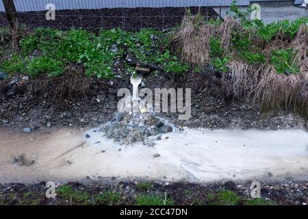 Verschmutztes Sturmwasser läuft von einem Industriegelände direkt in einen Entwässerungsgraben, Motueka, Neuseeland. Stockfoto
