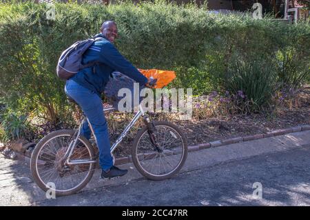 Alberton, Südafrika - unidentifizierter schwarzer Mann transportiert auf seinem Fahrrad-Bild einen Sack Feuerholz in horizontalem Format Stockfoto