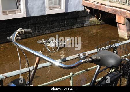 Gelehnt Fahrrad auf Metallgeländer des Freiburger Wasserkanals. Im fliessenden Wasser ist ein Skelett eines Fahrrades schwer beschädigt nicht mehr für den Einsatz geeignet. Stockfoto