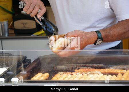 Ein Mann bereitet vor und eine gegrillte Wurst in einem Brot Brötchen mit gerösteten Zwiebel für einen Kunden in einem schnellen Imbissstand auf einem Marktplatz in Freiburg am Breisgau Stockfoto