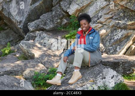 Portrait einer afrikanischen Frau, die auf Felsen sitzt und anschaut Kamera beim Wandern Stockfoto