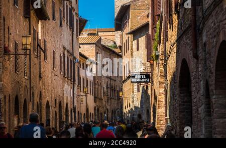 Schöne Aussicht auf die Via San Giovanni, die Hauptstraße der mittelalterlichen Stadt San Gimignano, Toskana, Italien. Viele Touristen gehen durch die Straße,... Stockfoto