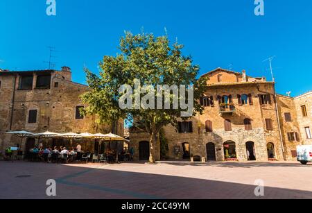 Herrliche Aussicht auf die Piazza delle Erbe neben der Stiftskirche Santa Maria Assunta in San Gimignano. Ein schöner Baum steht auf dem... Stockfoto