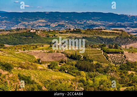 Atemberaubende Aussicht über die landwirtschaftlichen Täler in der Landschaft der mittelalterlichen Hügelstadt San Gimignano. Eine typische Landschaft mit Häusern, Olivenbäumen... Stockfoto