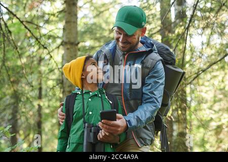 Lächelnder Vater zeigt seinem Sohn etwas auf dem Handy Während ihrer Wanderung im Wald Stockfoto