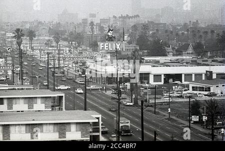 1964, historisch, sommerlich und ein Blick über eine trübe Skyline von Los Angles, mit Gebäuden, Autos, Straße und einem 'Felix'-Schild über einem Chevrolet-Autohaus. Stockfoto