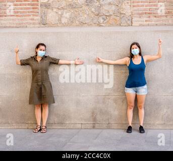 Zwei Frauen tragen schützende Gesichtsmasken stehen 2 m voneinander halten soziale Distanzierung Vermeidung der Ausbreitung von Coronavirus. Konzeptuelles Bild von Stockfoto