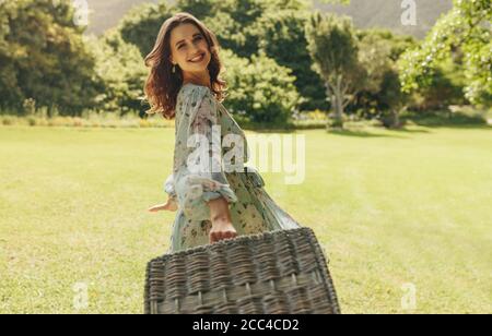 Schöne Frau mit Picknickkorb zu Fuß im Park. Hübsche Frau geht auf ein Wochenende Picknick. Stockfoto