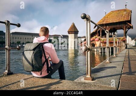 Junger Mann, der am Wasser sitzt und die Chapel Bridge in Luzern, Schweiz, betrachtet. Stockfoto