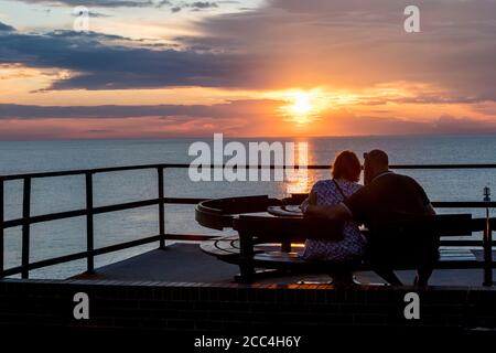 Paar beobachten den Sonnenuntergang über dem Meer an der Ostküste in Hunstanton. Stockfoto