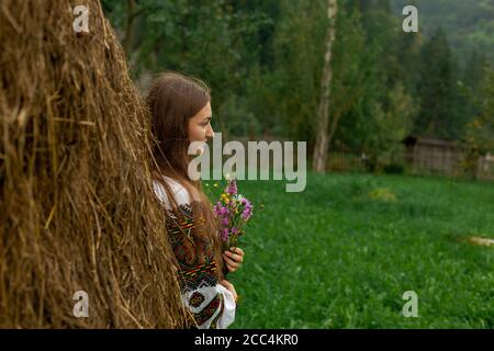 Mädchen mit lockeren Haaren mit einem Blumenstrauß steht Bei einem Heuhaufen Stockfoto