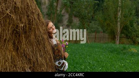 Mädchen mit lockeren Haaren mit einem Blumenstrauß steht Bei einem Heuhaufen Stockfoto