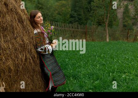 Mädchen mit lockeren Haaren mit einem Blumenstrauß steht Bei einem Heuhaufen Stockfoto