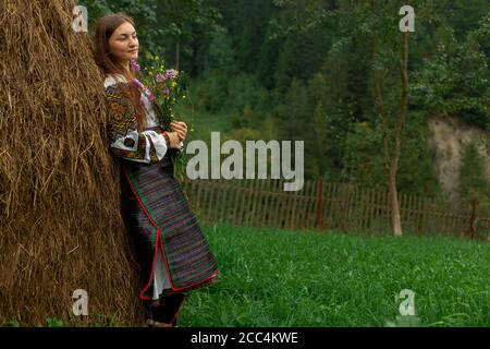 Mädchen mit lockeren Haaren mit einem Blumenstrauß steht Bei einem Heuhaufen Stockfoto