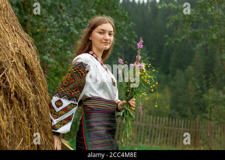 Mädchen mit lockeren Haaren mit einem Blumenstrauß steht Bei einem Heuhaufen Stockfoto