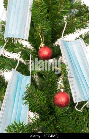 Vertikales Farbbild mit einer Vorderansicht eines Weihnachtsbaums, der mit roten Kugeln und blauen Coronavirus-Masken geschmückt ist. Covid und glückliches neues Jahr Konzept. Stockfoto