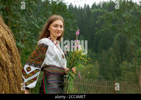 Mädchen mit lockeren Haaren mit einem Blumenstrauß steht Bei einem Heuhaufen Stockfoto