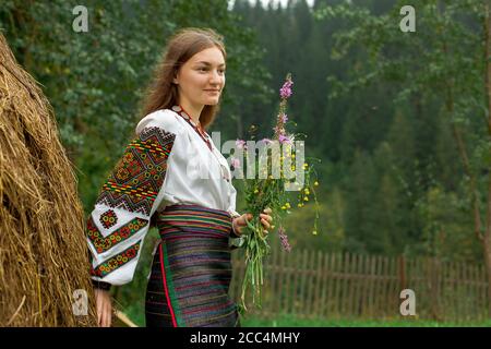 Mädchen mit lockeren Haaren mit einem Blumenstrauß steht Bei einem Heuhaufen Stockfoto