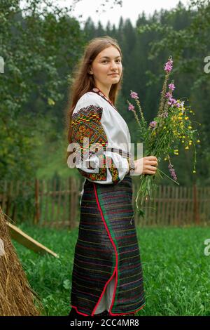 Mädchen mit lockeren Haaren mit einem Blumenstrauß steht Bei einem Heuhaufen Stockfoto