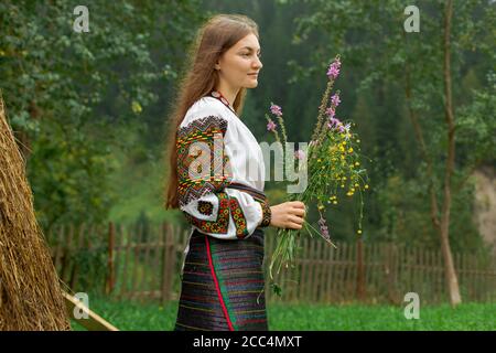 Mädchen mit lockeren Haaren mit einem Blumenstrauß steht Bei einem Heuhaufen Stockfoto