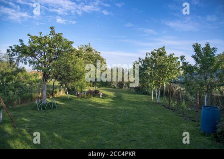 Sonnenuntergang und Schatten in einem wunderschön angelegten Dorfhof voller Grün. Stockfoto