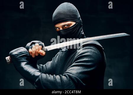 Kampf Ninja posiert mit einem Schwert über schwarzem Hintergrund. japanische Kämpfer Konzept Stockfoto