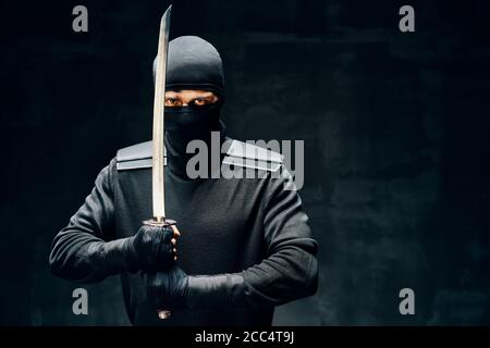 Kampf Ninja posiert mit einem Schwert über schwarzem Hintergrund. japanische Kämpfer Konzept Stockfoto