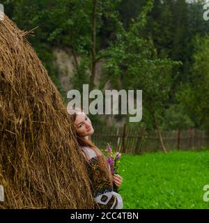 Mädchen mit lockeren Haaren mit einem Blumenstrauß steht Bei einem Heuhaufen Stockfoto