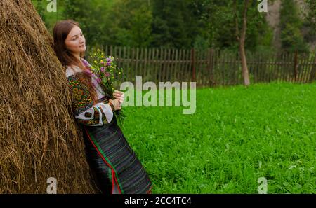 Mädchen mit lockeren Haaren mit einem Blumenstrauß steht Bei einem Heuhaufen Stockfoto
