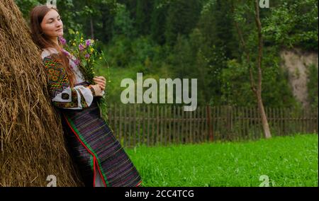 Mädchen mit lockeren Haaren mit einem Blumenstrauß steht Bei einem Heuhaufen Stockfoto