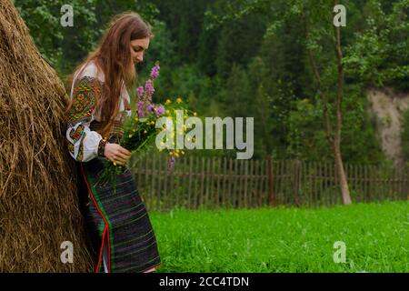 Mädchen mit lockeren Haaren mit einem Blumenstrauß steht Bei einem Heuhaufen Stockfoto