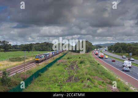 Direct Rail Services Klasse 88 BI-Modus Elektrische Lokomotive 88004 Schleppen eines Containerfrachtzuges auf der Hauptlinie der Westküste Über die Autobahn M6 Stockfoto