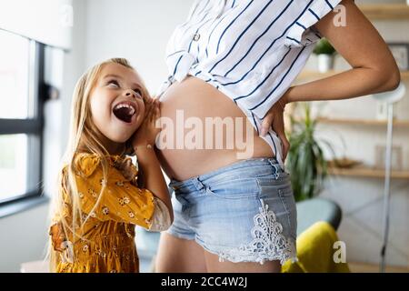 Frohe Familie. Schwangere Mutter und Tochter küssen entspannend zu Hause Stockfoto