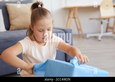 Mädchen mit Down-Syndrom zerreißt das Geschenkpapier auf der Box und ihr Geschenk zu Hause öffnen Stockfoto