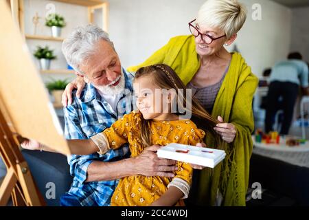 Ältere Menschen mit Kindermalerei auf Leinwand. Großeltern verbringen glückliche Zeit mit Enkelkind. Stockfoto