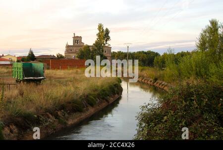 Blick auf den Canal de Pisuerga entworfen, um die zu bewässern Ackerland in Lantadila Palencia Spanien mit einem alten Bauerntrailer Und die Kirche Stockfoto