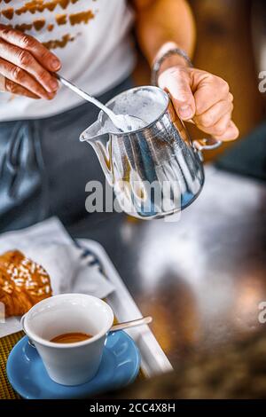 Hände der weiblichen Barista Gießen gedämpfte Milch aus Krug zu Cappuccinotasse Stockfoto