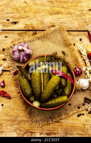 Marinierte Gurken mit Gewürzen und Kräutern. Traditionelle hausgemachte fermentierte Vorspeise in Tonschüssel. Alter Holztisch, Blick von oben Stockfoto
