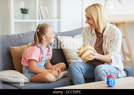 Glückliche Mutter zeigt ihr das Modell der Planeten Tochter mit Down-Syndrom und sie lachen, während sie sitzen Sofa zu Hause Stockfoto