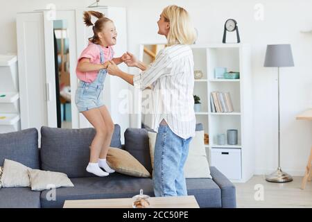 Mädchen mit Down-Syndrom springen auf dem Sofa sie spielt Mit ihrer Mutter, während sie zu Hause sind Stockfoto