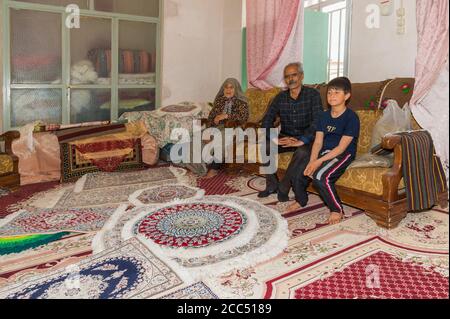 Iranische Familie sitzt auf einer Couch vor handgefertigten Teppichen, Na’in, Isfahan Provinz, Iran, Asien Stockfoto