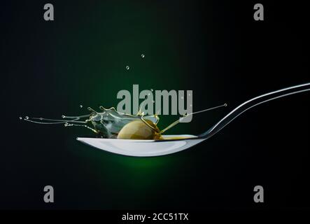 Nahaufnahme der grünen Olive mit Spritzöl auf einem Löffel Auf einem dunklen Hintergrund Stockfoto