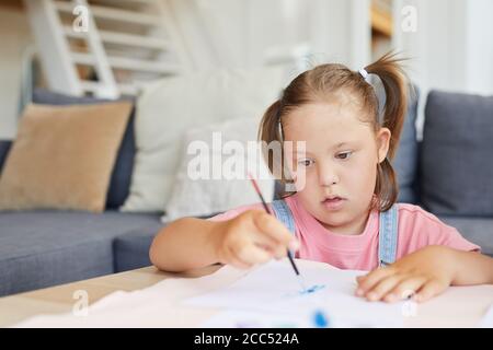Kleines Mädchen mit Down-Syndrom lernen, mit Farben zu malen Am Tisch zu Hause Stockfoto