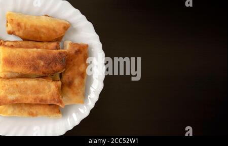 Berühmte traditionelle orientalische Küche, asiatische Küche. Gemüsefrühlingsrollen auf dunklem Holzhintergrund mit Kopierraum. Viele Frühlingsrollen auf weißem Teller. Oben Stockfoto