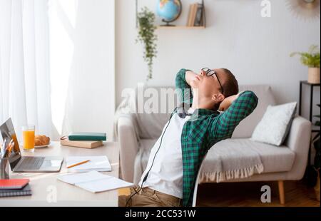 Schläfriger Schuler sitzt vor dem Laptop und Stretching Stockfoto